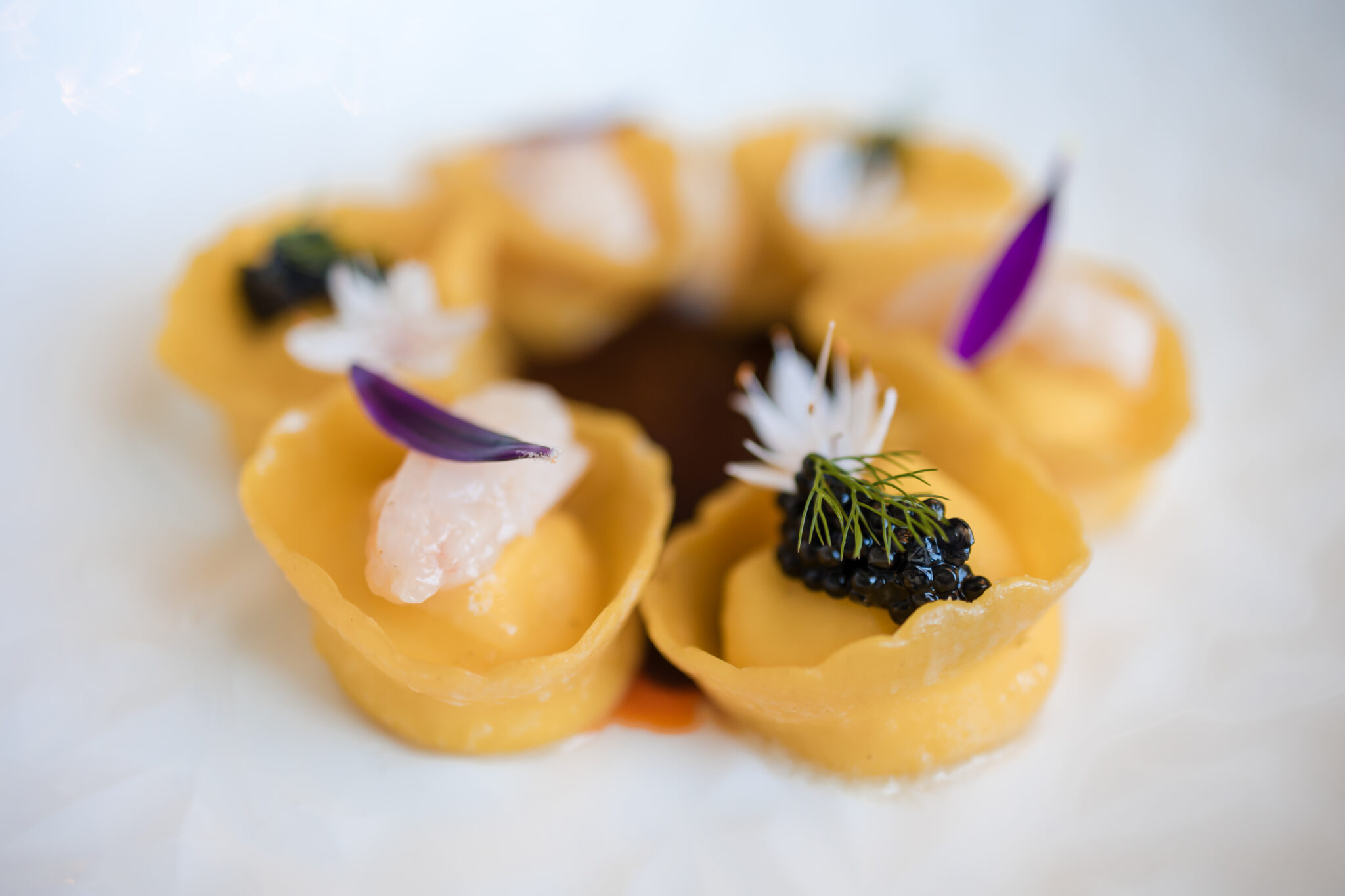 Primo piano di un piatto di cappellacci fatti a mano e sopra ogni cappellaccio è presente del caviale e tartare di scampi